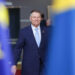 A man in a suit and tie running in front of EU and Swedish flags.
