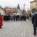 A woman in a red coat is standing in front of a group of Anti-Communist Political Prisoners.