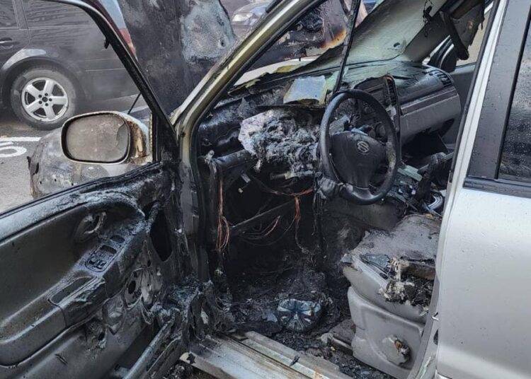 A burned-out car with the door open on Năsăud Street.